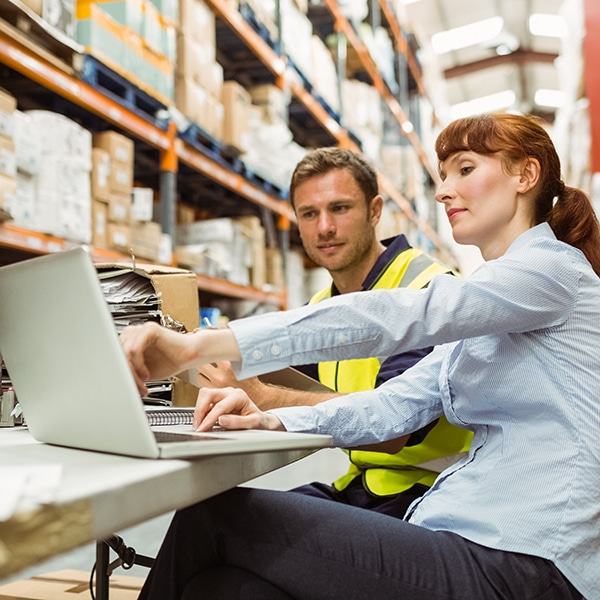 Warehouse worker and manager looking at laptop in a large warehouse